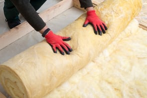 A worker rolling out fresh insulation material while wearing gloves.